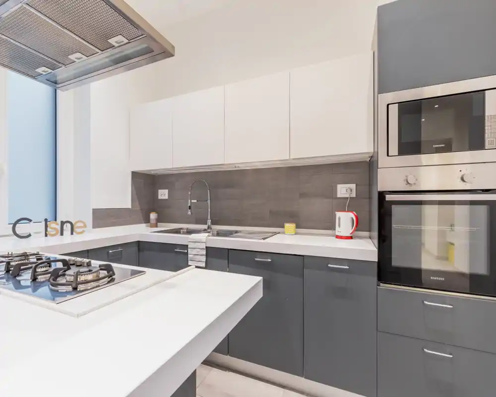 Cocina moderna y luminosa con placa de gas en isla, horno y microondas integrados, muebles bajos grises y armarios altos blancos: diseño limpio y contemporáneo perfecto para anuncios.