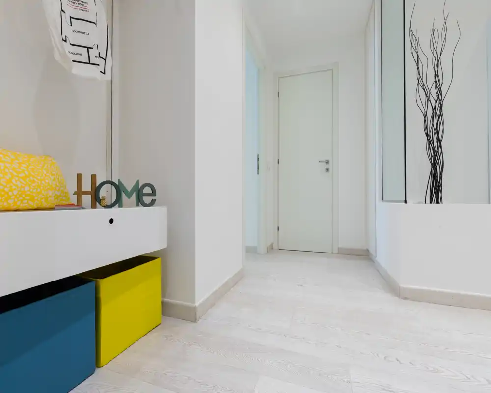 Entrada luminosa y moderna con suelo de madera clara, un banco con almacenamiento y detalles decorativos que crean una bienvenida agradable.