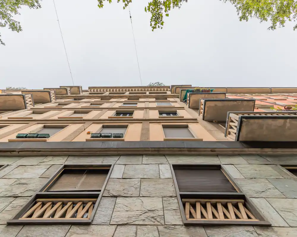 Vista en contrapicado de la fachada de un edificio de varios pisos con ventanas y balcones frente al cielo; la imagen muestra el exterior, no una habitación interior.
