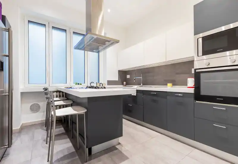 Cucina moderna e completa con isola centrale, elettrodomestici in acciaio inox e sgabelli — luminosa, pulita e ben organizzata per la vita contemporanea.