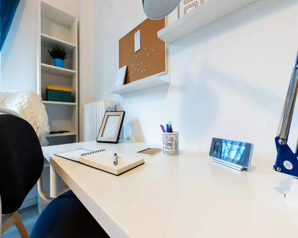 Bright, tidy home workspace with a white desk, notebook, lamp and shelving — ideal for remote work or study.