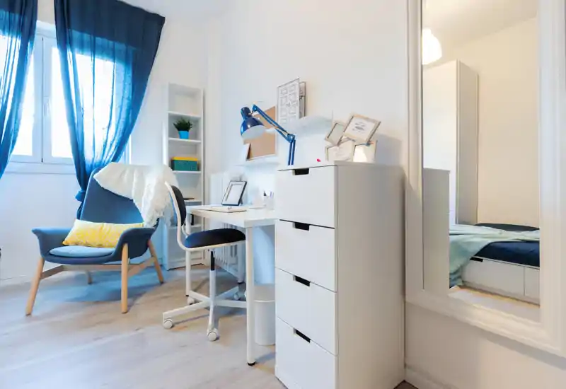Bright, stylish bedroom corner with a visible bed through the doorway, a cozy armchair and a compact workspace — ideal for a single renter or student.