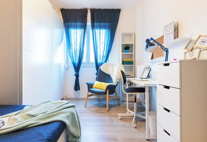 Bright, well-staged bedroom with a comfortable bed, cozy armchair and a small workspace by the window — ideal for single occupancy or a rental listing.