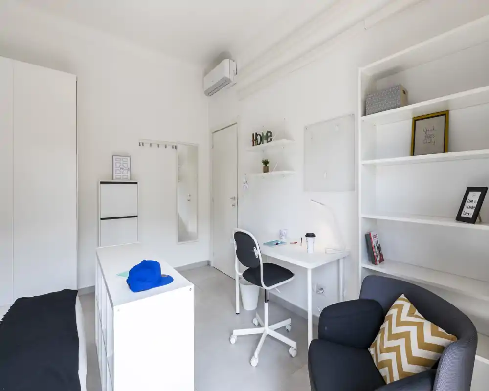 Dormitorio moderno y luminoso con cama individual, escritorio compacto y estanterías — espacio minimalista y bien iluminado, ideal para estudiantes o profesionales.