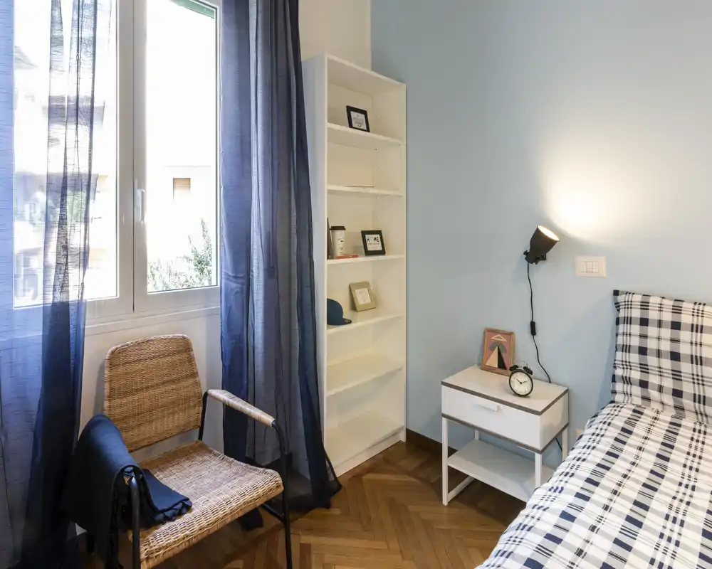 Rincón de dormitorio luminoso y bien decorado con cama individual, mesita y ventana con luz natural — ideal para anuncios de alquiler que destaquen una zona de descanso acogedora.