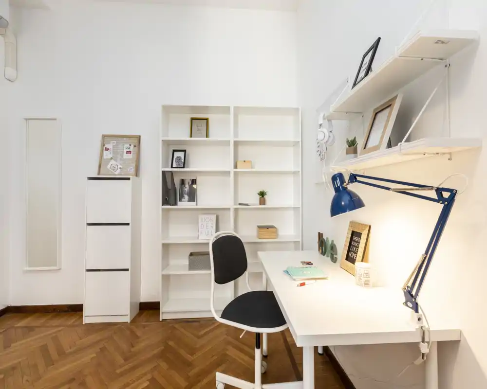 Rincón living/oficina luminoso y minimalista con escritorio blanco, estantería y lámpara de trabajo — ideal para un espacio de trabajo compacto.
