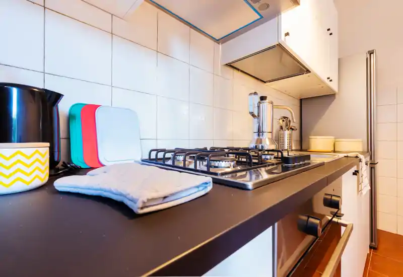 Encimera de cocina moderna bien equipada con vitro de gas, hervidor, tablas de cortar coloridas y accesorios; luminosa, ordenada y lista para cocinar.