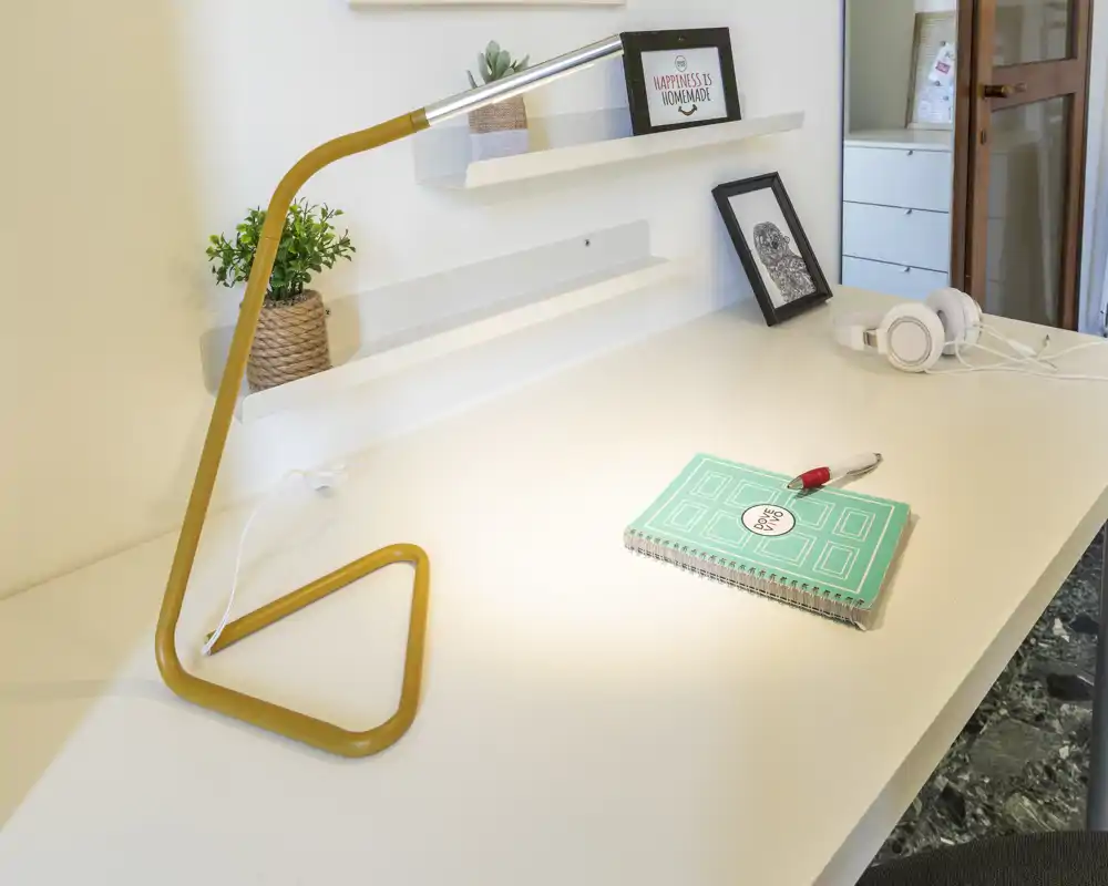 Rincón de trabajo moderno y luminoso con escritorio blanco, lámpara amarilla, libreta y detalles decorativos — ideal para estudiar o trabajar.