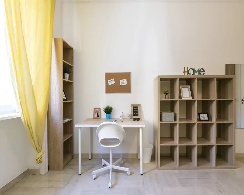 Espacio de trabajo luminoso y minimalista con escritorio blanco, silla giratoria y estanterías de madera: la luz natural y las cortinas amarillas crean un rincón acogedor.