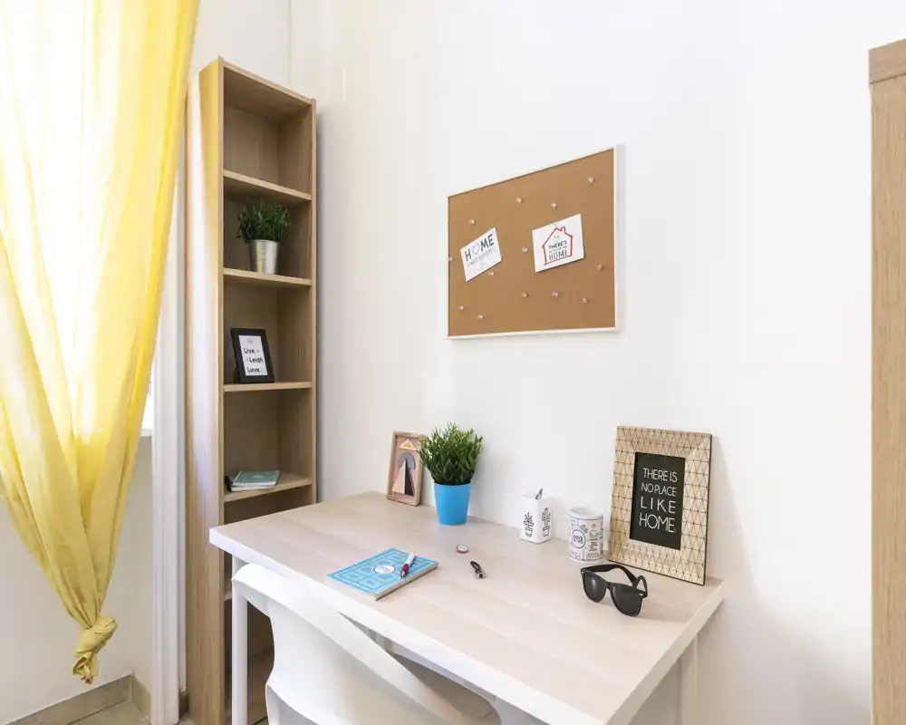 Área de escritorio luminosa y ordenada con mesa de madera clara, planta en maceta y marcos decorativos — ideal para una pequeña oficina en casa o rincón de estudio.