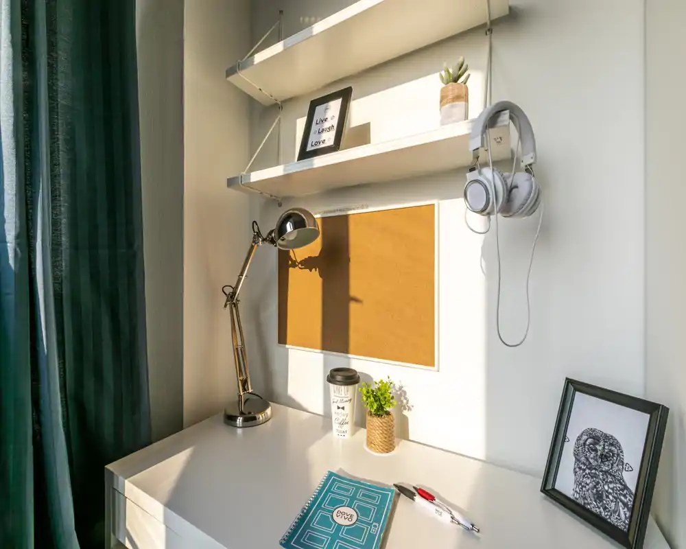 Rincón de estudio luminoso y ordenado con escritorio blanco, corcho para notas, lámpara regulable, auriculares colgados y plantas decorativas — perfecto para estudiar o trabajar.