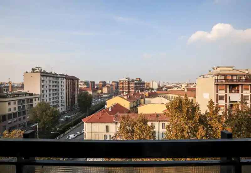Vista dal balcone su un quartiere residenziale con tetti in cotto e alberi autunnali; panorama luminoso ideale per la luce del mattino.