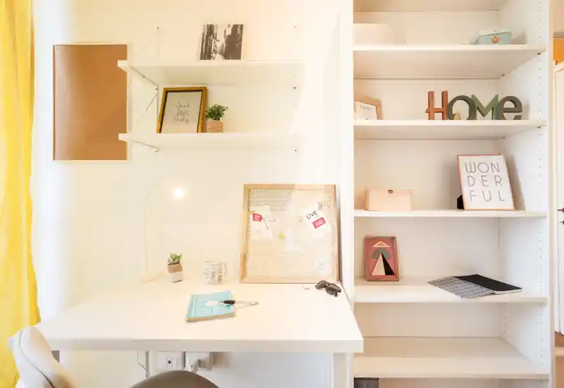 Angolo studio luminoso e ordinato con scrivania bianca, lampada, scaffalatura e decorazioni — ideale per studio o lavoro da remoto.