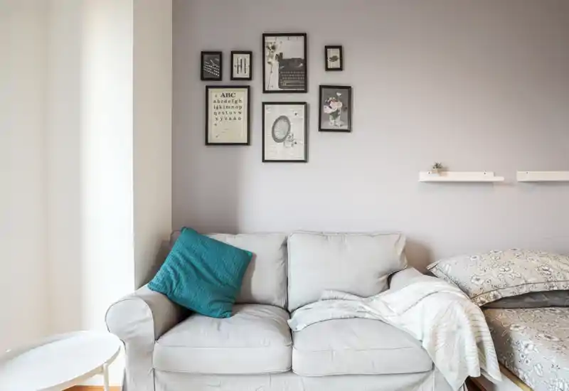 Zona living luminosa e curata con un divano a due posti, cuscino decorativo e quadri a parete; allestimento accogliente adatto a foto per affitti.