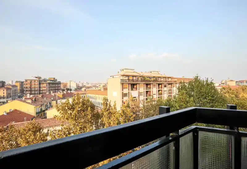 Balcone soleggiato con vista nitida sugli edifici residenziali e le chiome degli alberi, ideale per rilassarsi all'aperto.