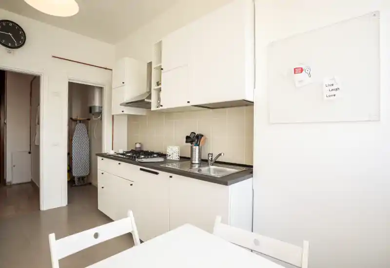 Cucina compatta e luminosa con mobili bianchi, piano cottura a gas e piccolo tavolo da pranzo — ordinata e pronta all'uso.