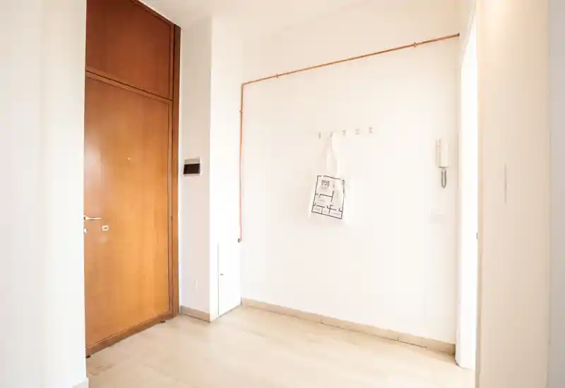 Ingresso luminoso e minimale con porta d'ingresso in legno, appendiabiti a parete e citofono — un'area d'ingresso pulita adatta per gli annunci.