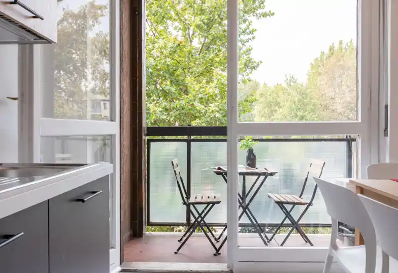 Balcone arredato con un tavolino da bistrò e due sedie pieghevoli, affacciato su un verde paesaggio: luminoso e perfetto per il caffè mattutino.