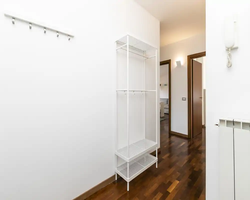 Entrada/pasillo minimalista y bien iluminado con ganchos de pared y un armario abierto estrecho; suelo de madera pulida y puertas hacia otras estancias.