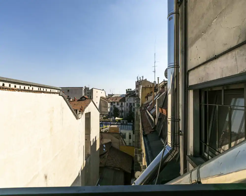 Vista urbana soleada desde un balcón con tejados cercanos y cielo azul — perfecta para resaltar el paisaje de la ciudad y la luz natural.