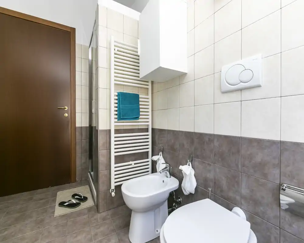 Baño moderno con azulejos, inodoro, bidé y toallero calefactor mural; espacio luminoso, limpio y funcional.