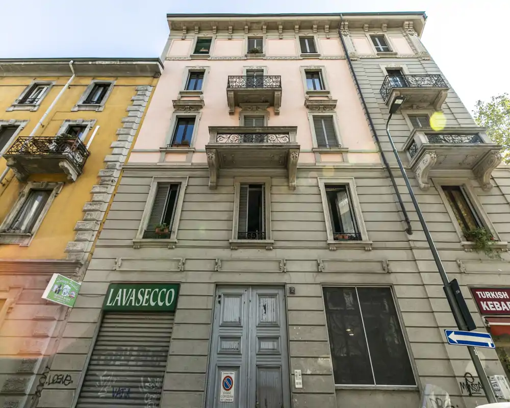 Vista exterior de la fachada de un edificio de varios pisos con balcones y locales en planta baja, incluida una señal de lavandería; fotografía diurna nítida, adecuada para mostrar el edificio o el frente de la calle.