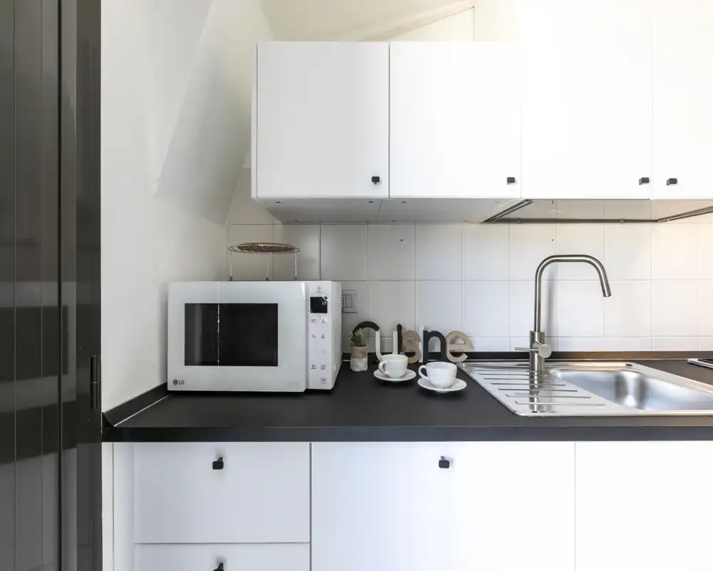 Encimera de cocina moderna y luminosa con fregadero integrado, grifo de acero inoxidable y microondas sobre una superficie negra limpia; pequeños detalles decorativos crean un espacio funcional y ordenado.