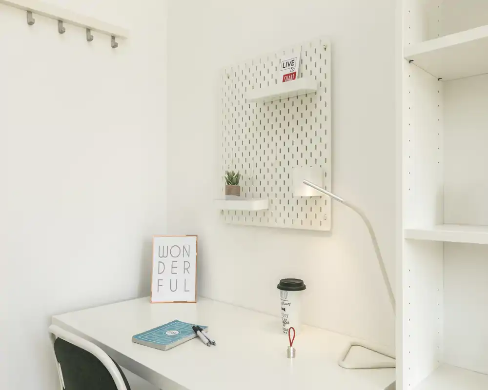 Coin bureau minimaliste et lumineux avec bureau blanc, lampe de travail, petite plante et étagères — idéal pour travailler ou lire.
