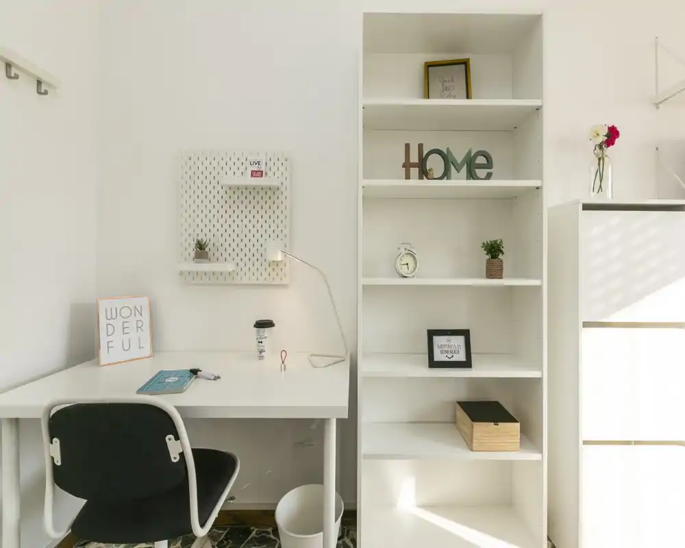 Coin bureau lumineux et minimaliste avec bureau blanc, lampe de travail, étagère et quelques éléments décoratifs — idéal pour un petit bureau à domicile.