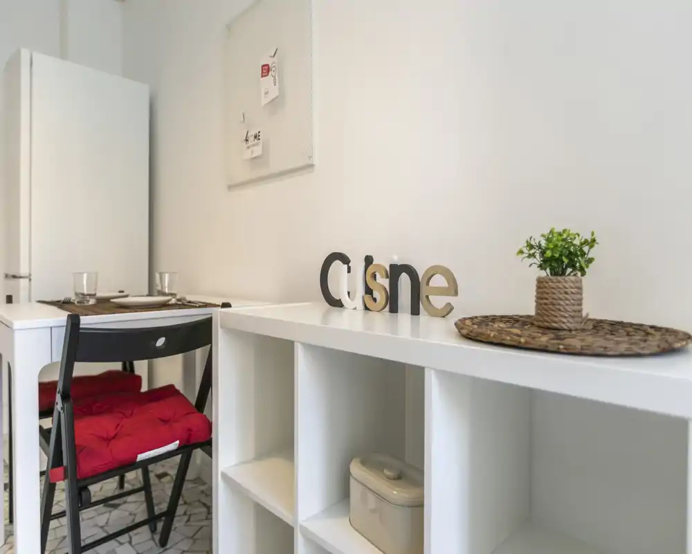 Coin cuisine moderne et compact avec plan de travail blanc, petite table et éléments décoratifs apportant une ambiance lumineuse et accueillante.