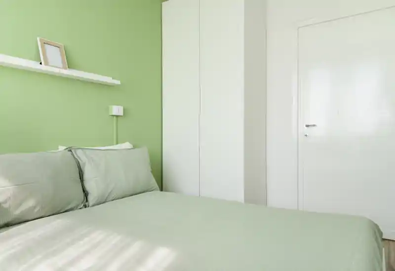Camera da letto luminosa e minimal con parete verde, letto matrimoniale ben rifatto e armadio bianco alto — semplice, ariosa e ideale per annunci.