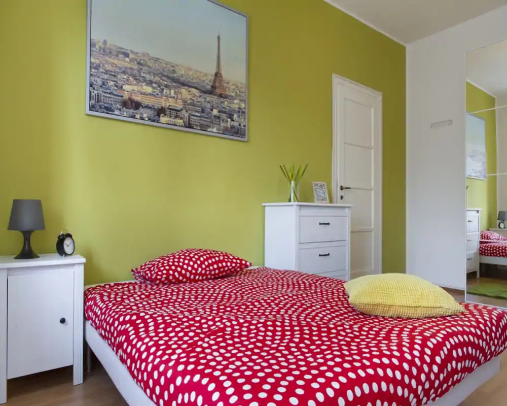 Dormitorio luminoso y moderno con edredón rojo de lunares, mesita de noche y cómoda; decoración fresca y gran cuadro sobre la cama.