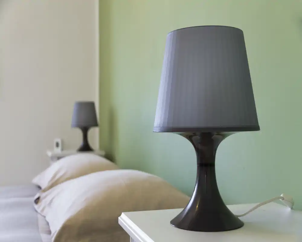 Detalle de un dormitorio luminoso y moderno con dos lámparas de mesita y almohadas visibles: primer plano que destaca la iluminación y la zona de cama acogedora.