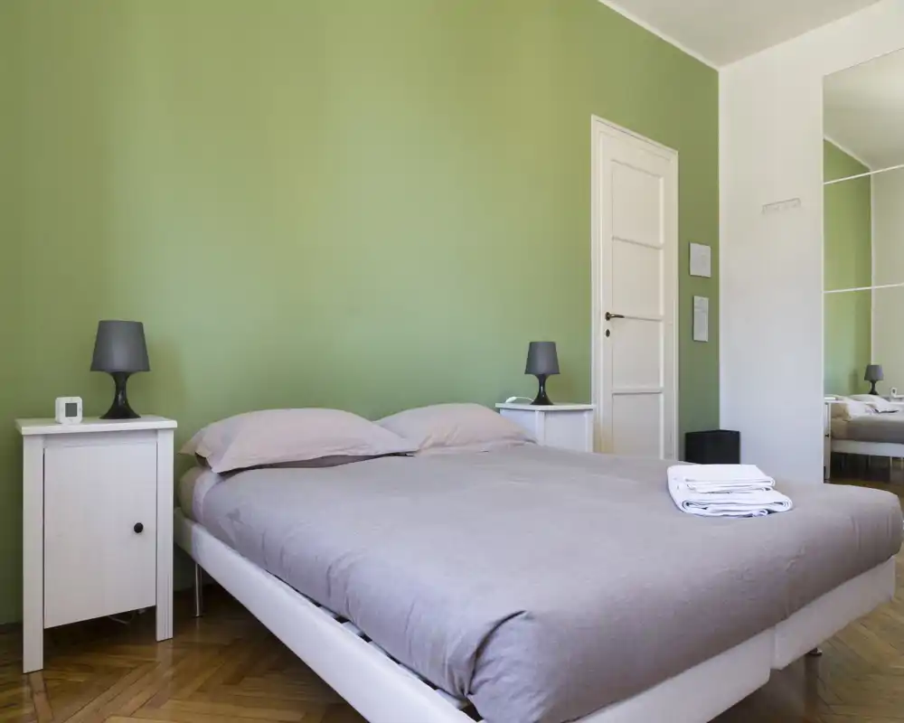 Dormitorio luminoso y moderno con una amplia cama doble, ropa de cama suave y mesitas a juego con lámparas. La decoración sobria y la luz natural crean un ambiente tranquilo y acogedor, ideal para el anuncio.