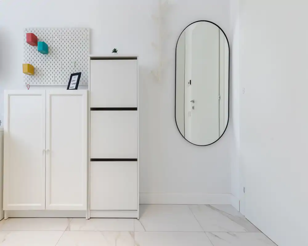 Bright, minimal entrance with white storage cabinets, a tall mirror and tiled floor — clean and welcoming first impression.