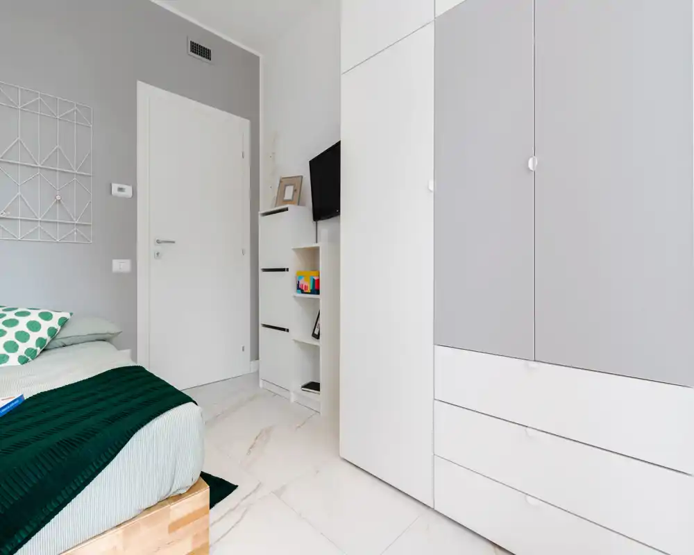 Camera da letto moderna e luminosa con letto confortevole, tessili verdi e grande armadio bianco. Lo spazio è minimal e ben illuminato, perfetto per un soggiorno tranquillo.