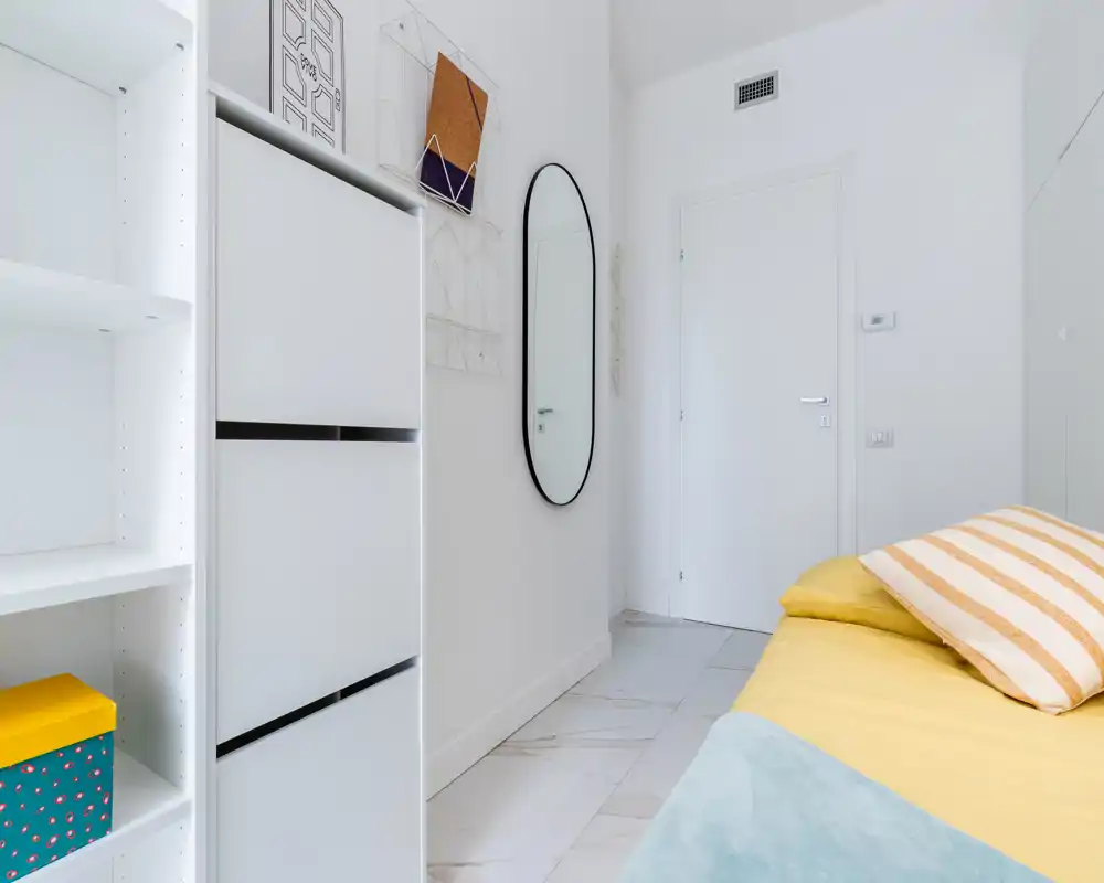 Bright, modern bedroom corner with a yellow bedspread, striped pillow and clean white storage units; minimal, airy styling ideal for a rental listing.