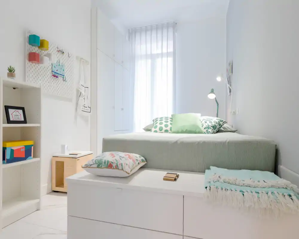 Dormitorio moderno y luminoso con cama doble bien arreglada, textiles verdes y cojines decorativos; la luz natural entra por las cortinas translúcidas creando un ambiente tranquilo y aireado.
