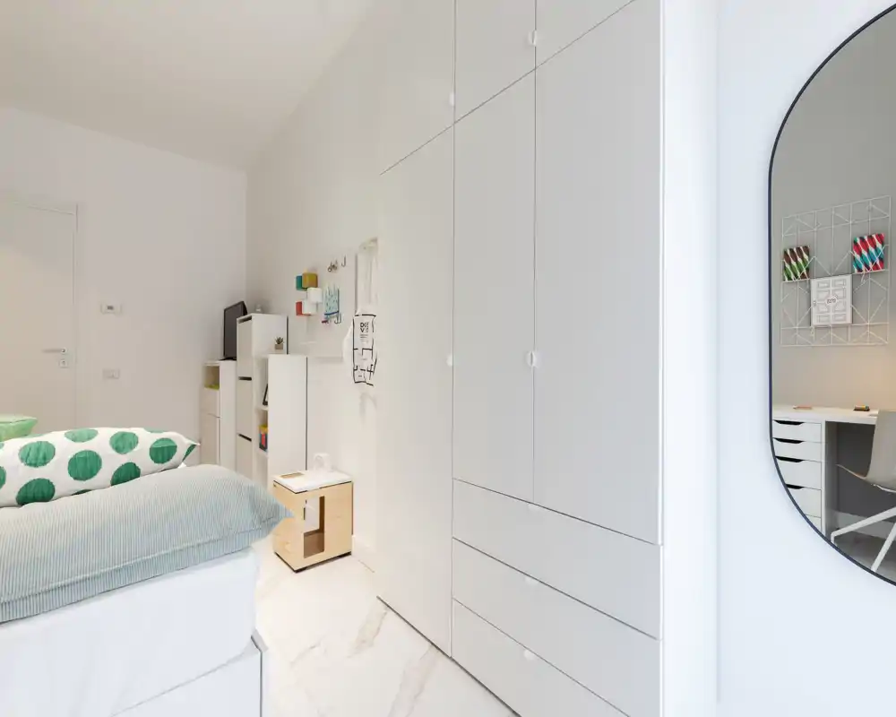 Dormitorio moderno y luminoso con armario empotrado blanco, cama cómoda con cojines estampados y mesita de almacenamiento; estilo minimalista y un pequeño espacio de trabajo reflejado en el espejo.