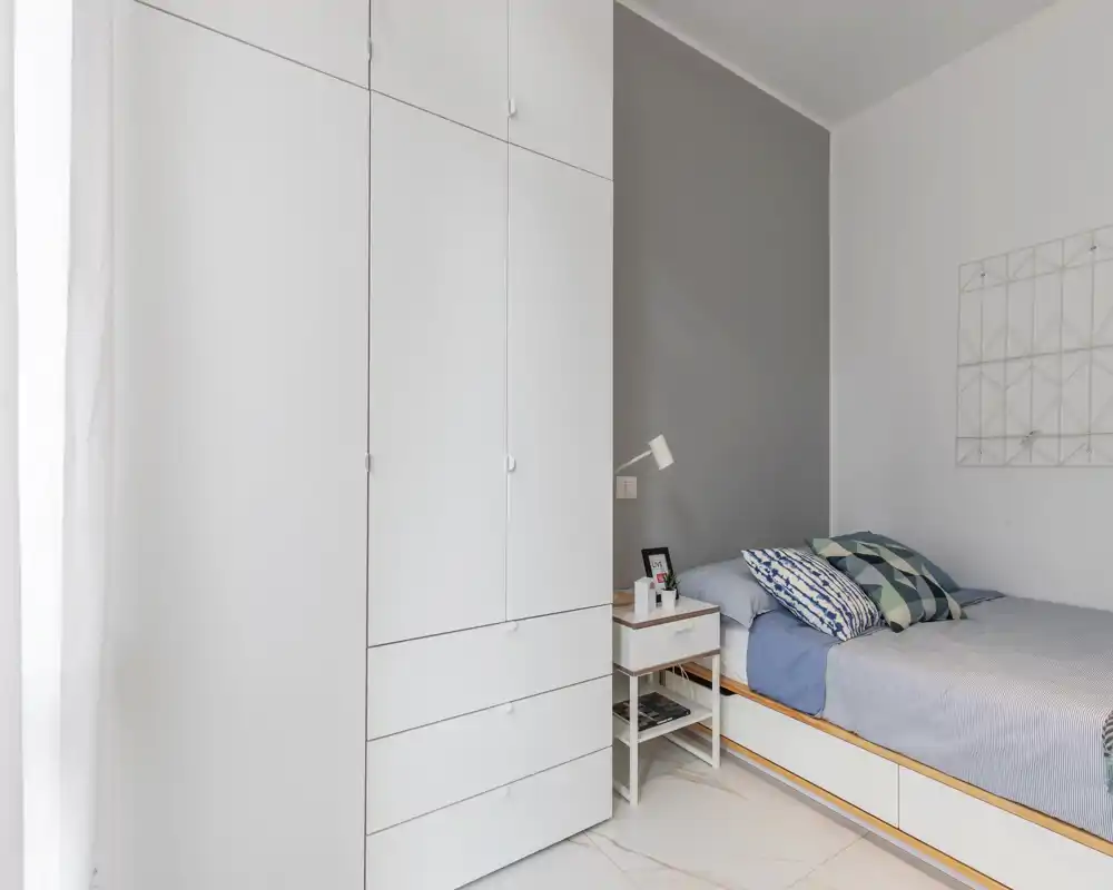 Dormitorio moderno y luminoso con cama bien hecha, cojines decorativos y un armario empotrado blanco que aporta un estilo minimalista y limpio.