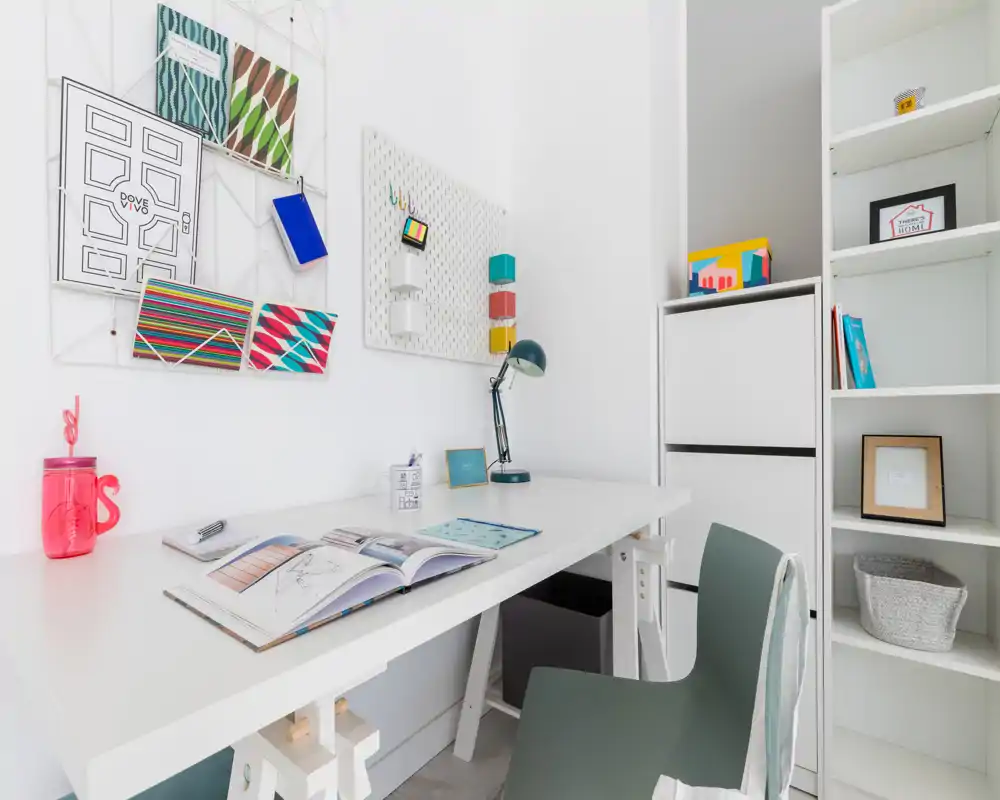 Espacio de trabajo moderno y luminoso con escritorio blanco, silla cómoda y estanterías ordenadas — accesorios coloridos y organizadores en la pared hacen de este rincón de oficina en casa un lugar funcional y acogedor.