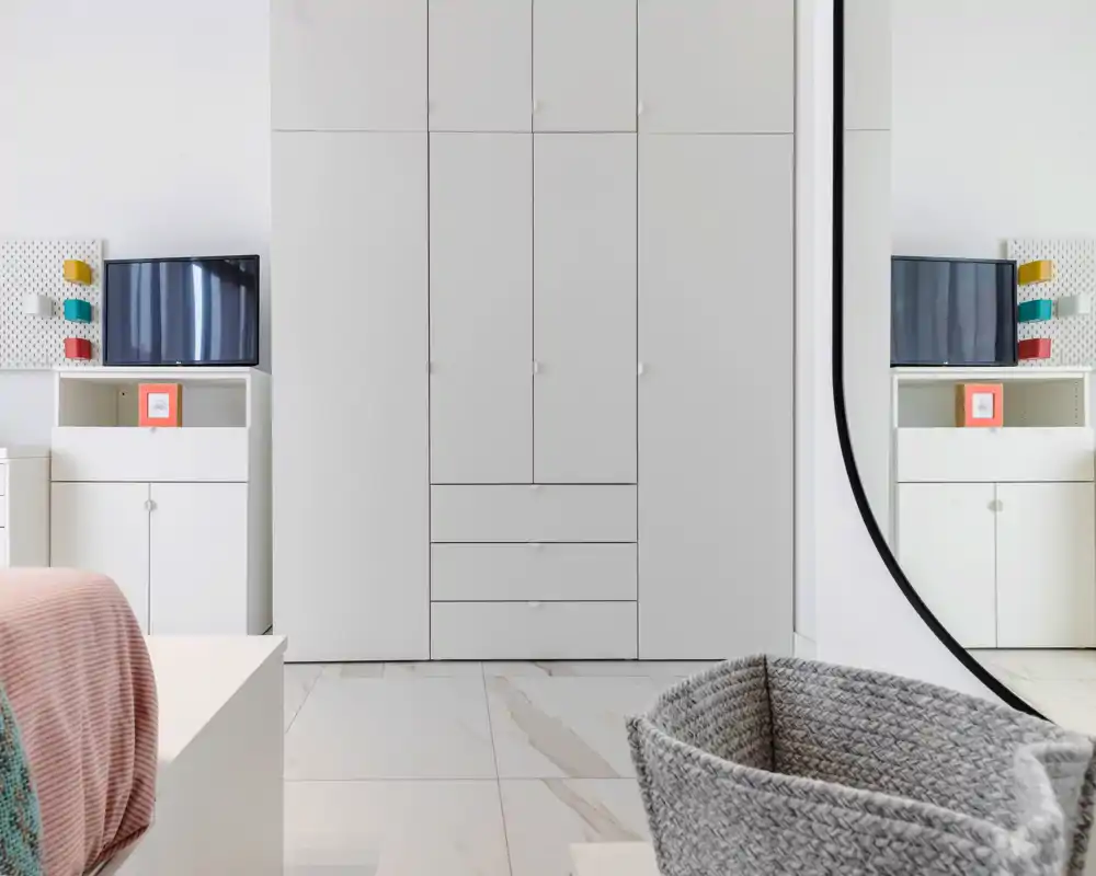 Rincón de dormitorio moderno y luminoso con cama parcialmente visible, armario empotrado blanco, mesitas y una cesta tejida — estilo limpio y minimalista ideal para el anuncio.