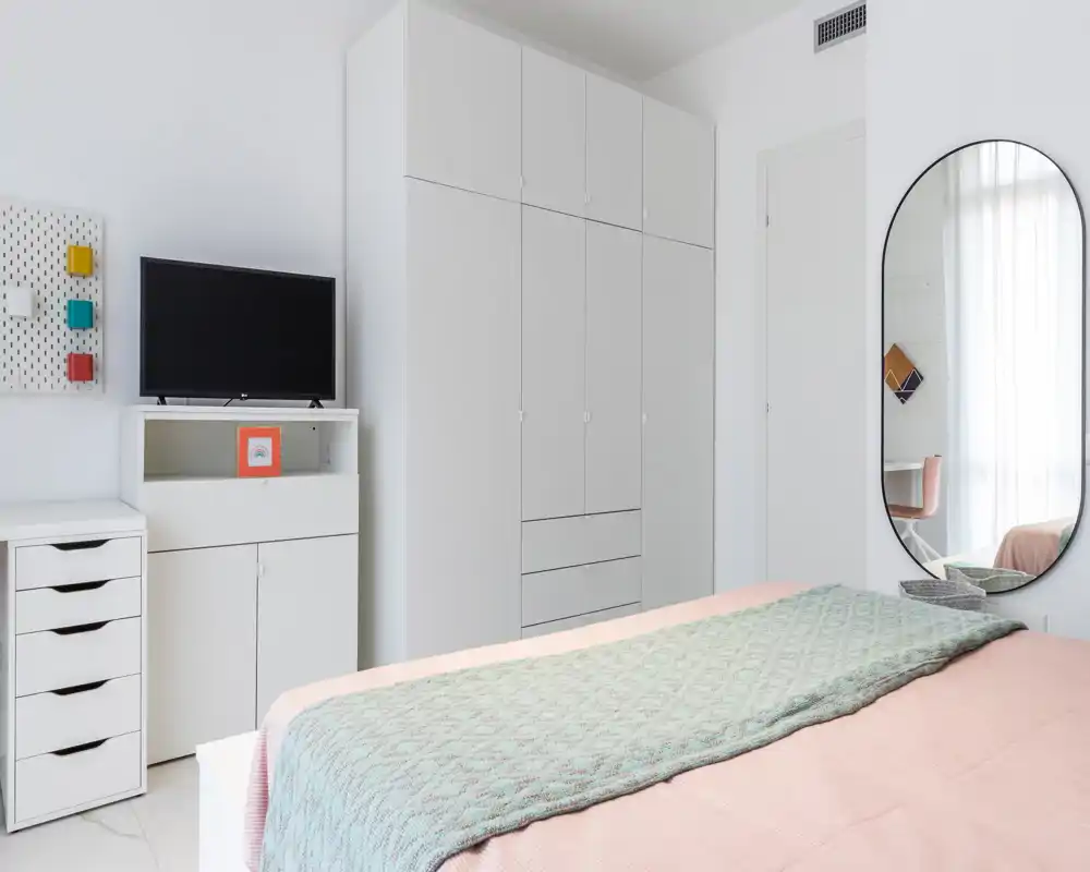 Dormitorio moderno y luminoso con cama bien hecha, armarios empotrados grandes y un espejo de cuerpo entero que amplifica la luz.