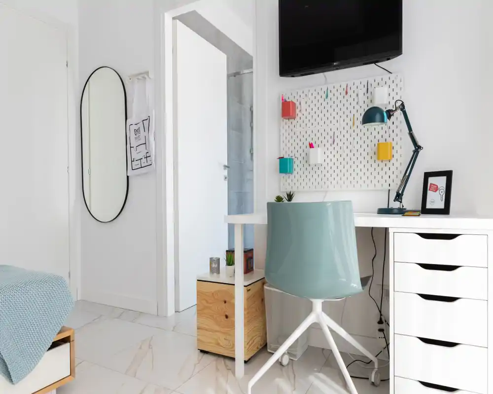 Bright, modern bedroom corner with a visible bed edge, a tidy desk and stylish chair — ideal for a single occupant or work-from-home setup.