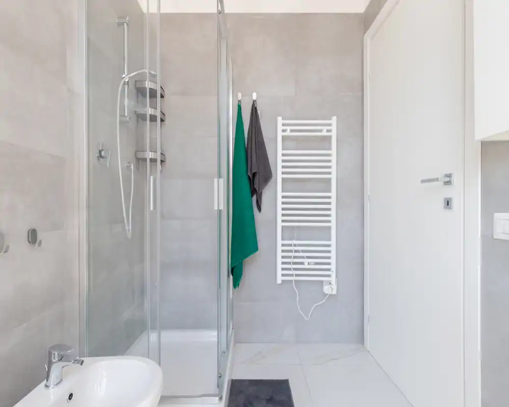 Bagno moderno con cabina doccia in vetro, scaldasalviette a parete e lavabo, in toni chiari e neutri.