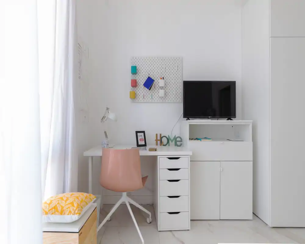 Coin lumineux et minimaliste bureau/salon avec bureau blanc, chaise pivotante rose et petit meuble TV — un espace moderne et soigné idéal pour télétravailler ou se détendre.
