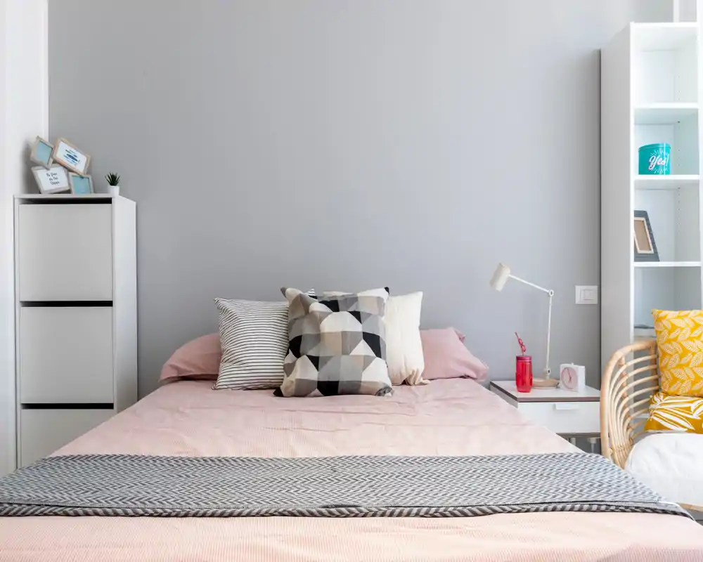 Chambre lumineuse et moderne avec un lit bien fait, coussins décoratifs et tons pastel apportant une ambiance calme et accueillante.