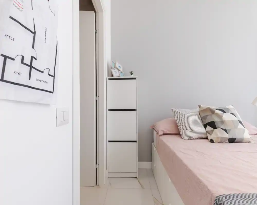 Chambre lumineuse et minimaliste avec un lit bien fait, coussins géométriques et linge de lit rose pâle créant une ambiance moderne et apaisante.