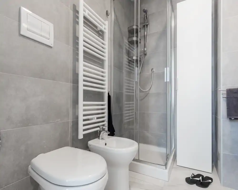 Salle de bain compacte et moderne avec WC, bidet et douche d'angle fermée par une paroi vitrée ; carrelage gris et sanitaires blancs pour un style épuré.