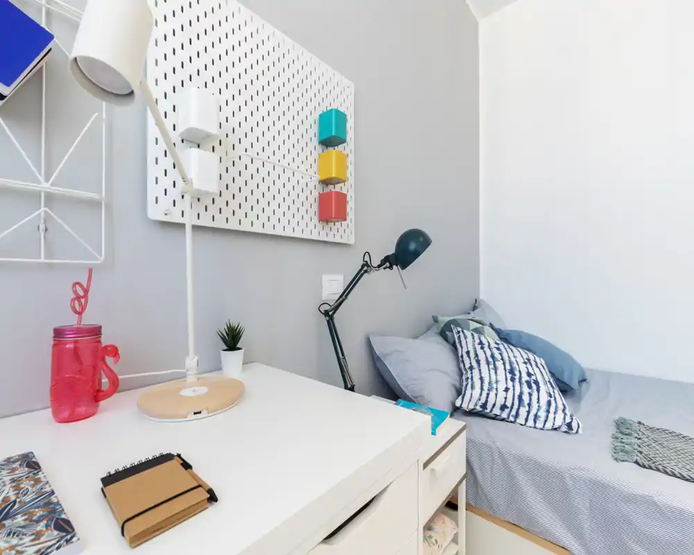 Compact, tidy bedroom corner with a single bed, soft linens and a study desk; bright, well-styled and suitable for a rental listing.